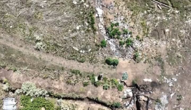 A Ukrainian drone drops munitions on a Russian soldier carrying multiple water bottles. He falls, then eventually gets up and moves into a dugout, where more grenades follow.