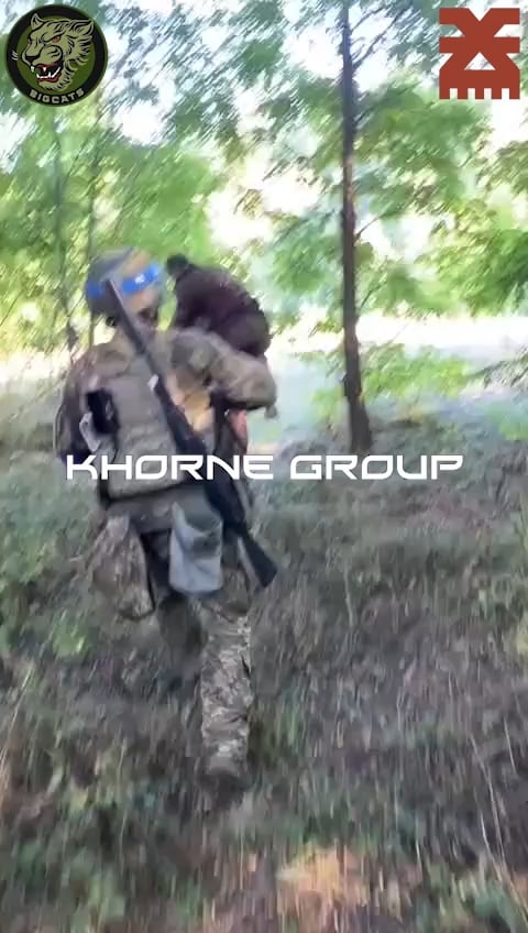 Ukranian soldier from Khorne group carrying wounded russian soldier on his back somewhere in Kursk region (don't ask about yellow tactical shorts)