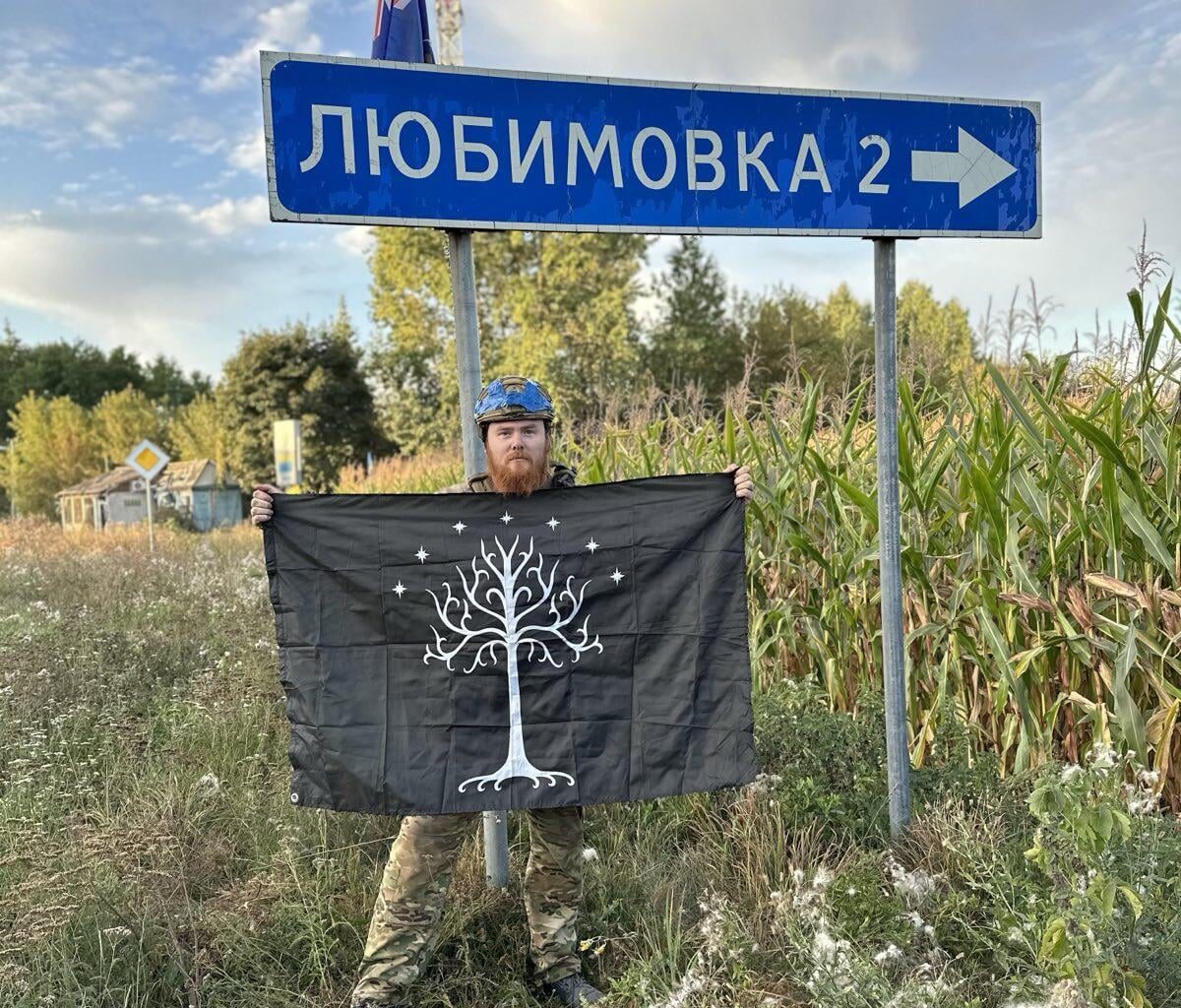 Volunteer soldier from New Zealand - with his country’s flag, and the Flag of Gondor, in the International Legion of the Ukrainian Army - standing by a road sign, Kursk Oblast.