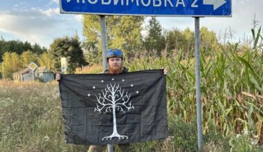 Volunteer soldier from New Zealand - with his country’s flag, and the Flag of Gondor, in the International Legion of the Ukrainian Army - standing by a road sign, Kursk Oblast.