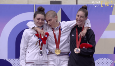 What a shot! Silver and bronze medalists help Marie Patouillet, gold medalist, standing up during her anthem