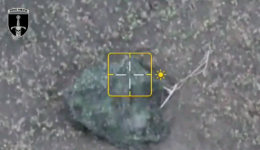 Two Russian soldiers trying to cross a field under a camouflaged net and being attacked by UAV-dropped munitions.