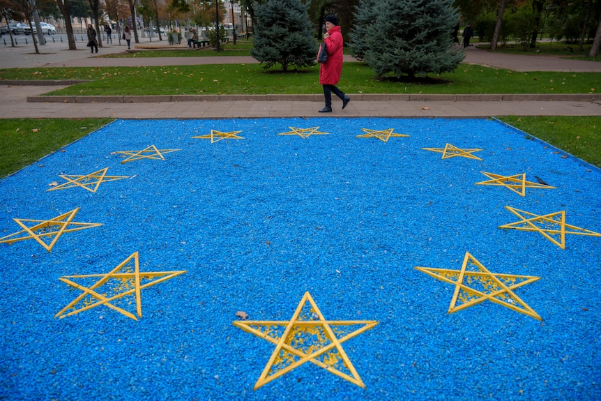 A woman walks by a European Union flag made of blue pebbles.