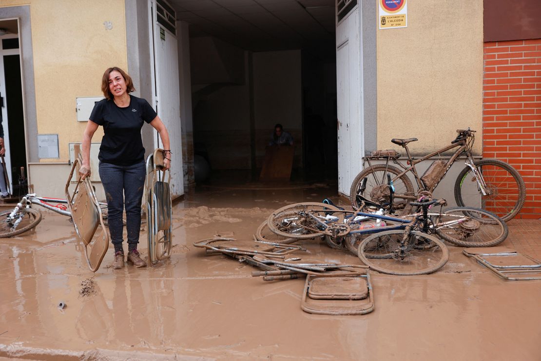 A woman carries chairs caked in mud after torrential rains caused flooding in La Alcudia, in Spain's Valencia region.