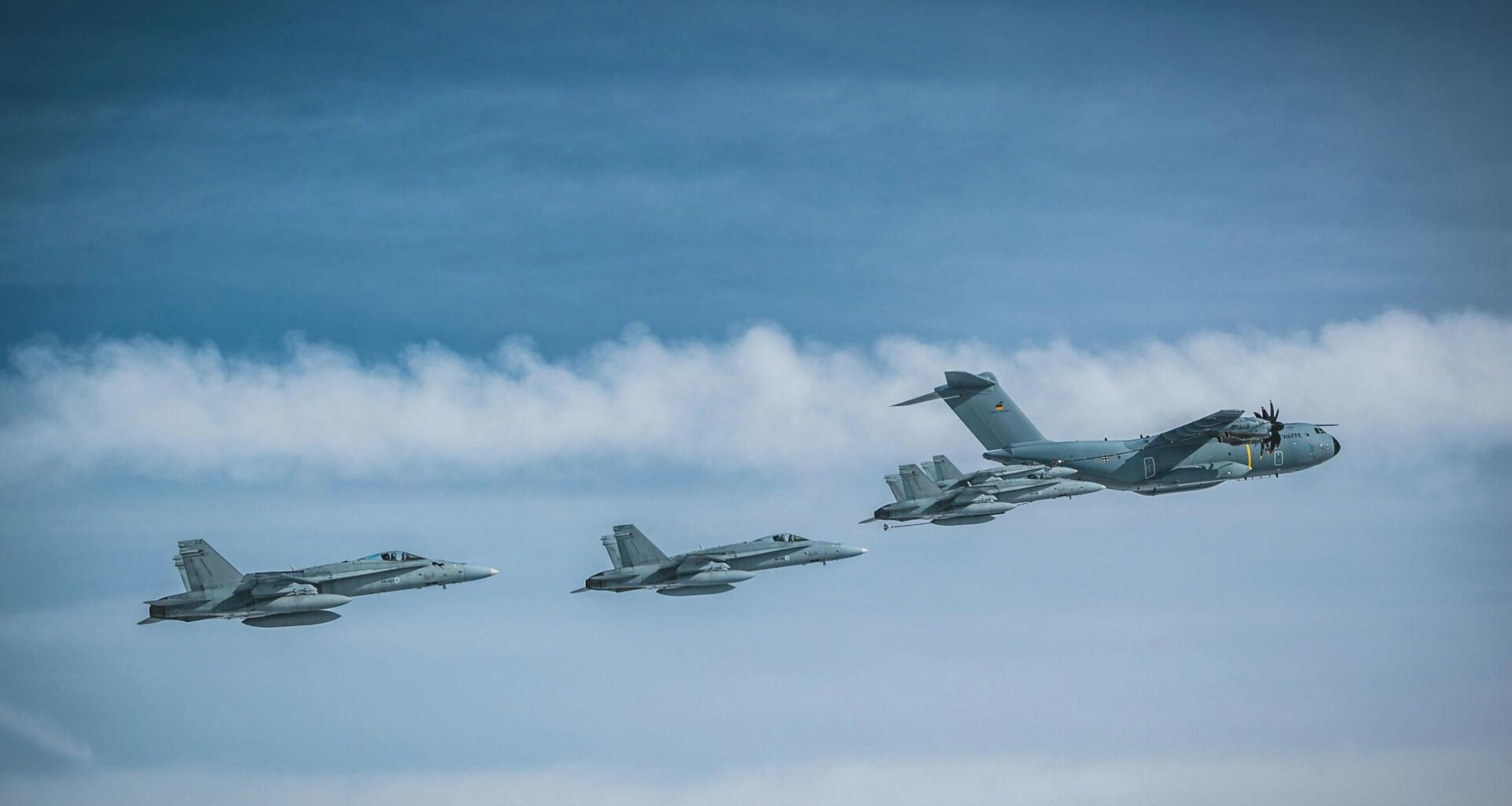 A German Air Force Airbus A400M Atlas flies in formation with four Finnish F/A-18 fighters.