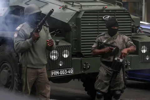 Reuters Two masked Mozambican police officers try to disperse people gathering to take part a march called by presidential candidate Venâncio Mondlane over the killing of two his supporters, in Maputo, Mozambique - Monday 21 October 2024