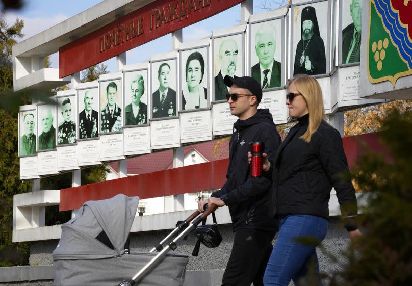 A couple walk past a billboard with portraits of honorary residents of the city in Tiraspol, 31 October 2021