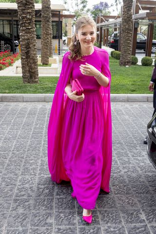 Princess Elisabeth wearing a hot pink gown with a cape and matching shoes as she walks outside near palm trees