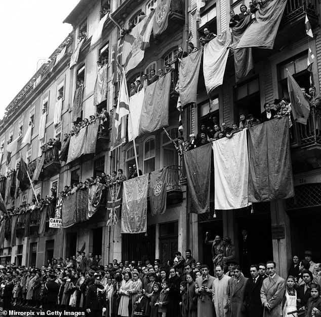 Residents in Portugal hang flags from their windows as they wait to greet the Queen