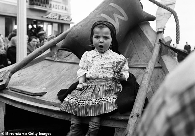 A young girl sits on an old fishing boat to try to get a glimpse of the Queen at Nazare village in 1957