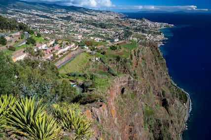 Blick vom Aussichtspunkt Cabo Girao auf Madeira über die begrünte Steilküste, die Häuser von Funchal und den blauen Atlantik