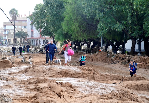 Miembros de la familia caminan por una calle cubierta de barro en una zona inundada en Picanya, cerca de Valencia, este de España, el 30 de octubre de 2024. (Foto de José Jordán/AFP).