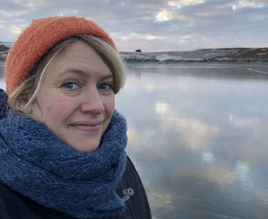 Valgerður Pálmadóttir in a hat and scarf by a lake