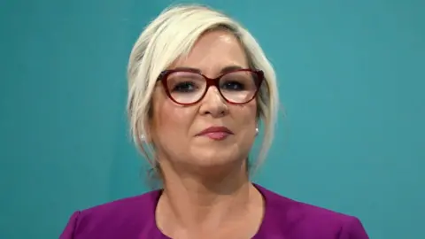 Getty Images Michelle O'Neill - she has blonde hair and is wearing a purple top and red-rimmed glasses.