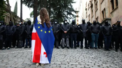 EPA A girl draped in a Georgian and European flag stands facing a dozen men dressed in black