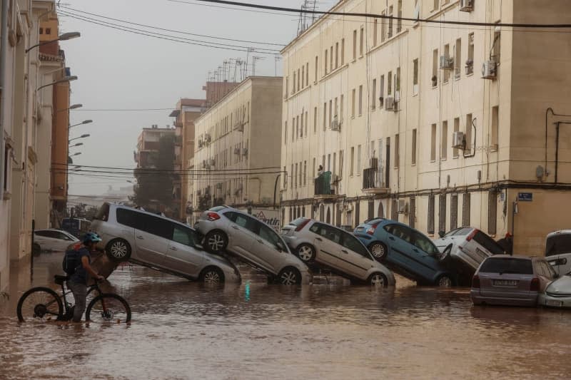 A man rides his bycicle as he passes by destroyed cars in the La Torre neighborhood. At least 51 people have died in the severe storms in Spain, specifically in the Mediterranean region of Valencia, the Spanish news agency Europa Press reported on 30 October, citing the regional government in Valencia. Rober Solsona/EUROPA PRESS/dpa