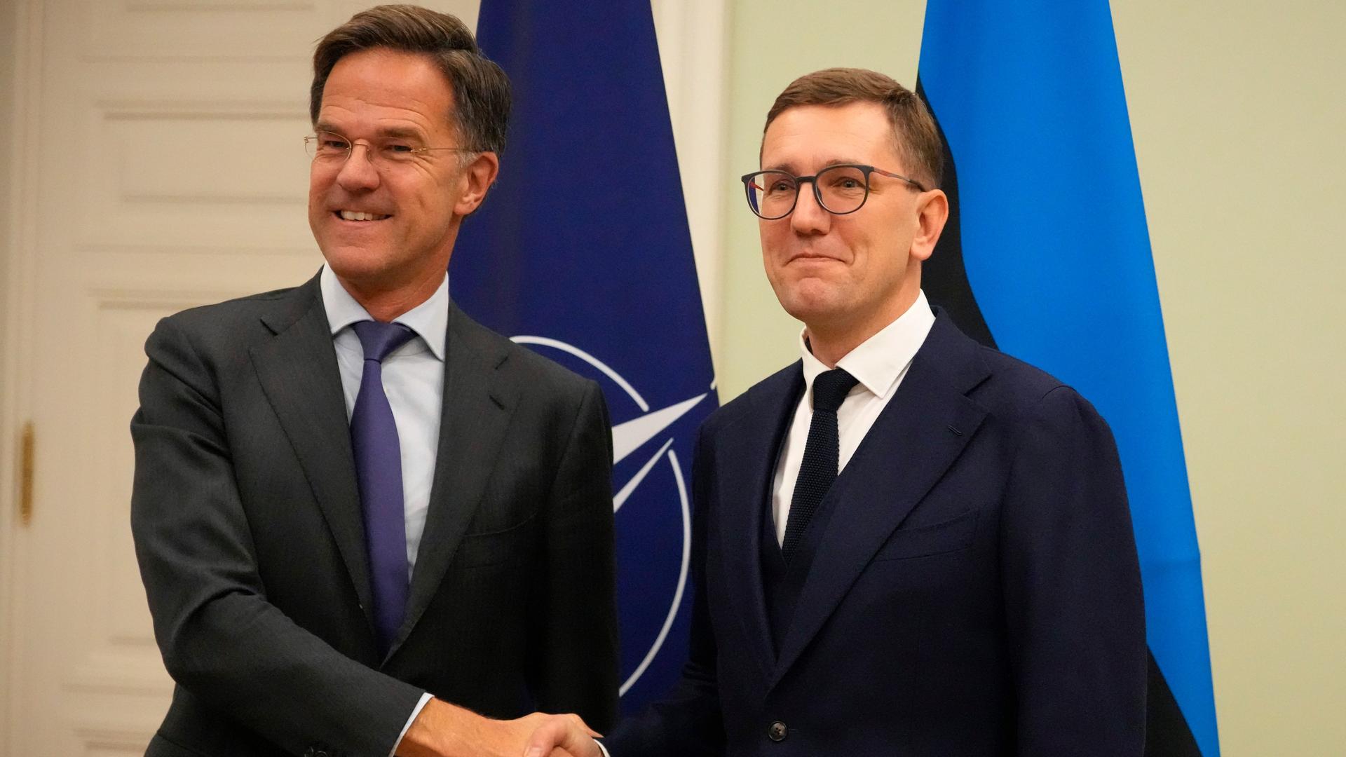 Der estnische Premierminister Kristen Michal und NATO-Generalsekretär Mark Rutte schütteln in Tallinn Hände. Im Hintergrund sind die Flaggen des Verteidigungsbündnisses sowie Estlands zu sehen.