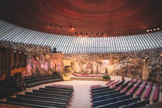 The famous Temppeliaukio Rock Church in Helsinki with light pouring in through the glass, reflecting off the rock walls and copper ceiling