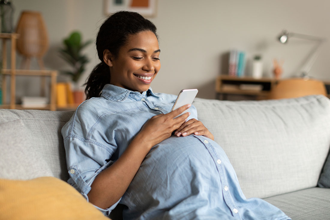 Pregnant Black woman sitting on a couch looking at her cell phone