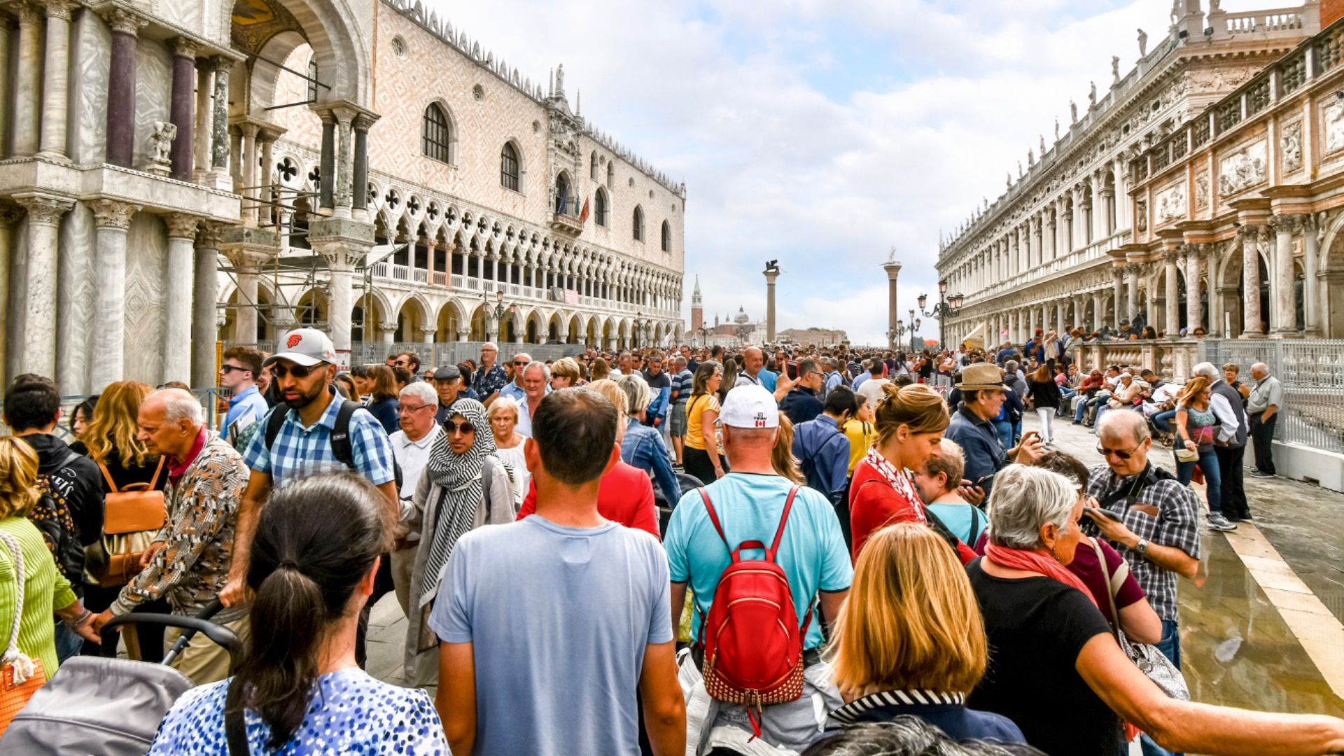 The visible effects of overtourism as cruise ship passengers crowd the walkway at the Doge's Palace in Piazza San Marco on a busy day in Venice, Italy