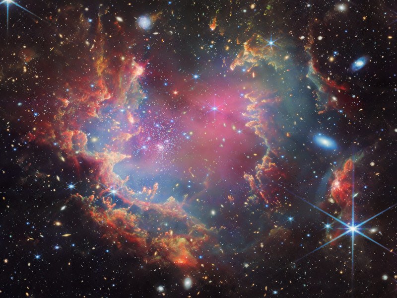 A star cluster is shown inside a large nebula of many-coloured gas and dust.