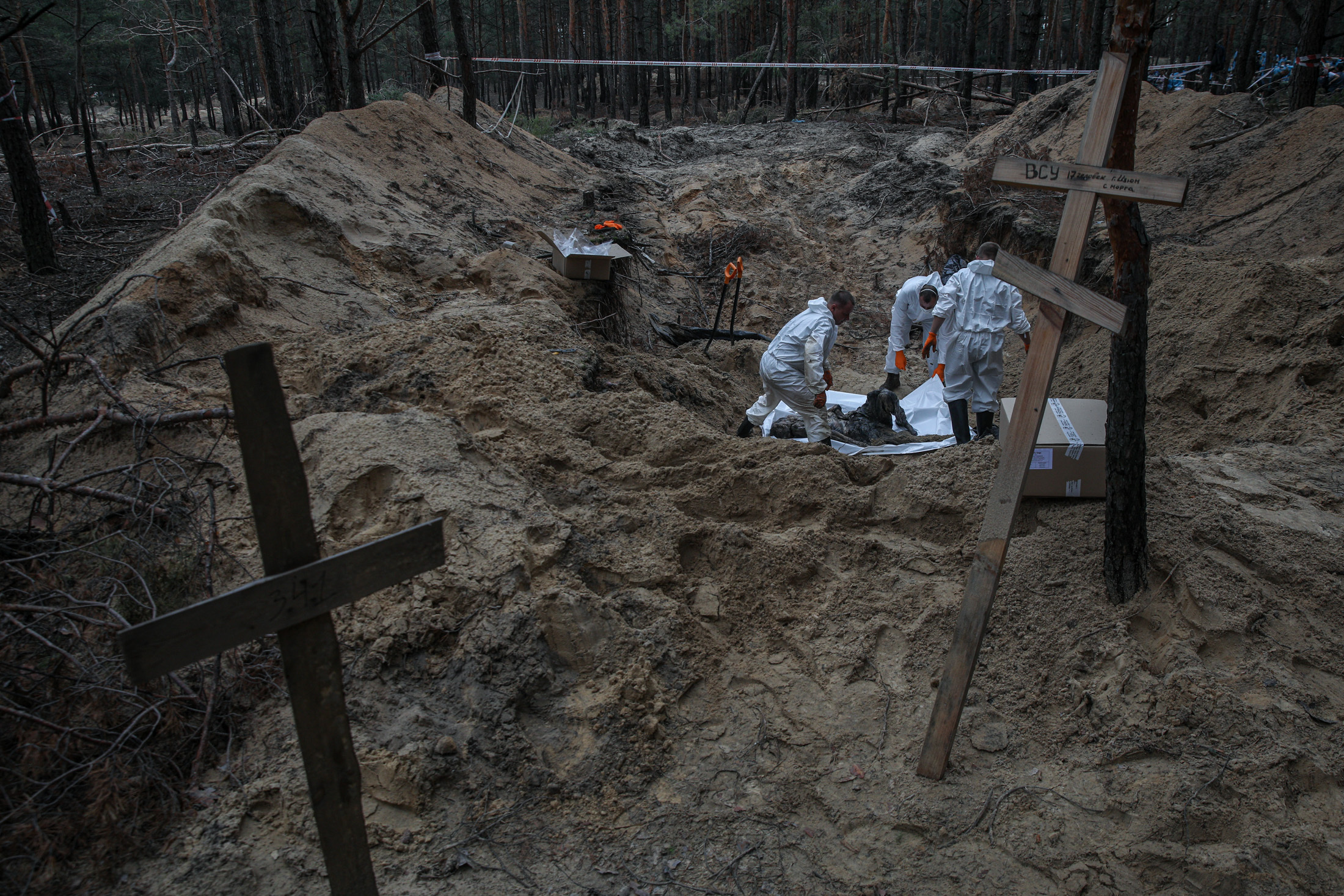 Workers exhume a body at a mass burial site containing around 440 graves in liberated Izium, Kharkiv Oblast, on Sept. 16, 2022.