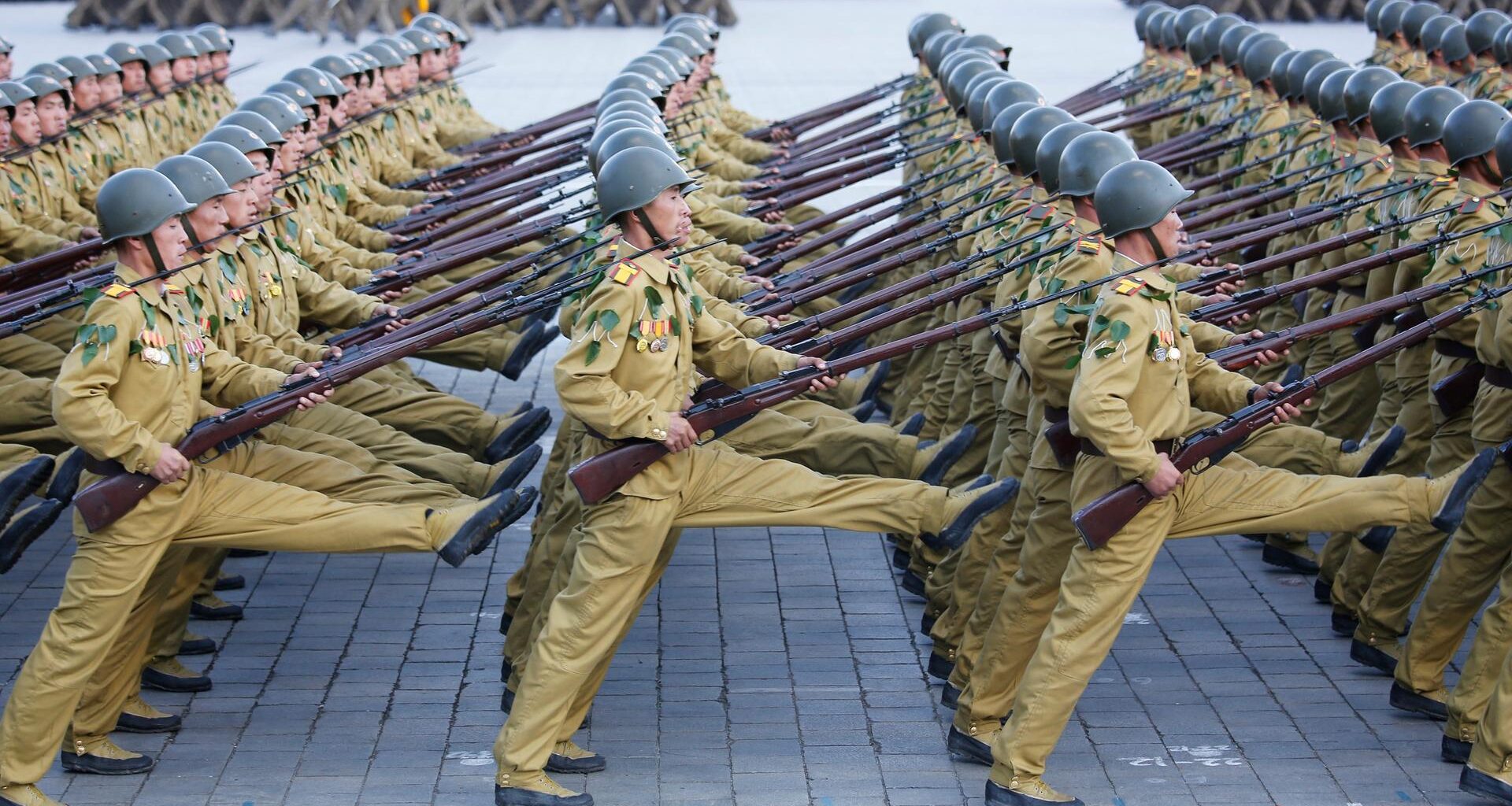 Die Soldaten gehen in mehreren Reihen hintereinander im Stechschritt über einen Platz. Sie tragen Gewehre.