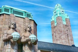 Two statues holding globes in front of the granite and turquoise facade of the Helsinki Central Railway Station