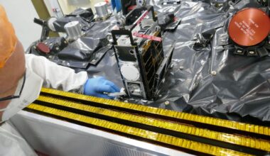 A metal rack of computer components are stacked in a cubesat on a table covered in a black tarp.