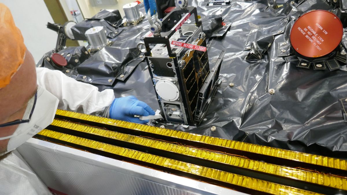 A metal rack of computer components are stacked in a cubesat on a table covered in a black tarp.