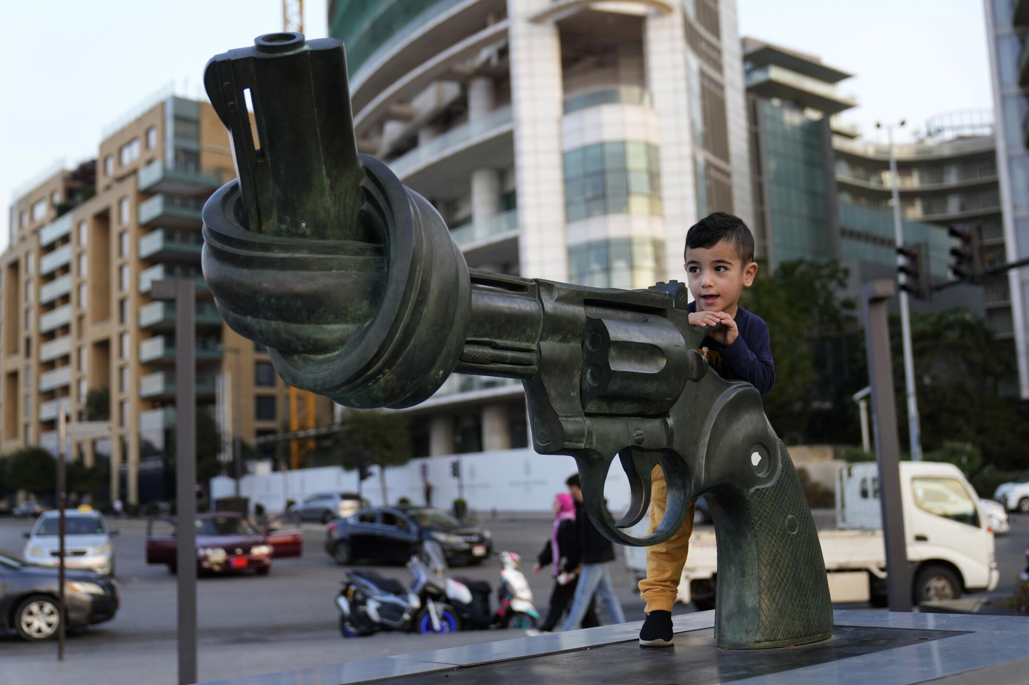 A boy climbs on a statue of a giant pistol whose barrel has been tied in a knot