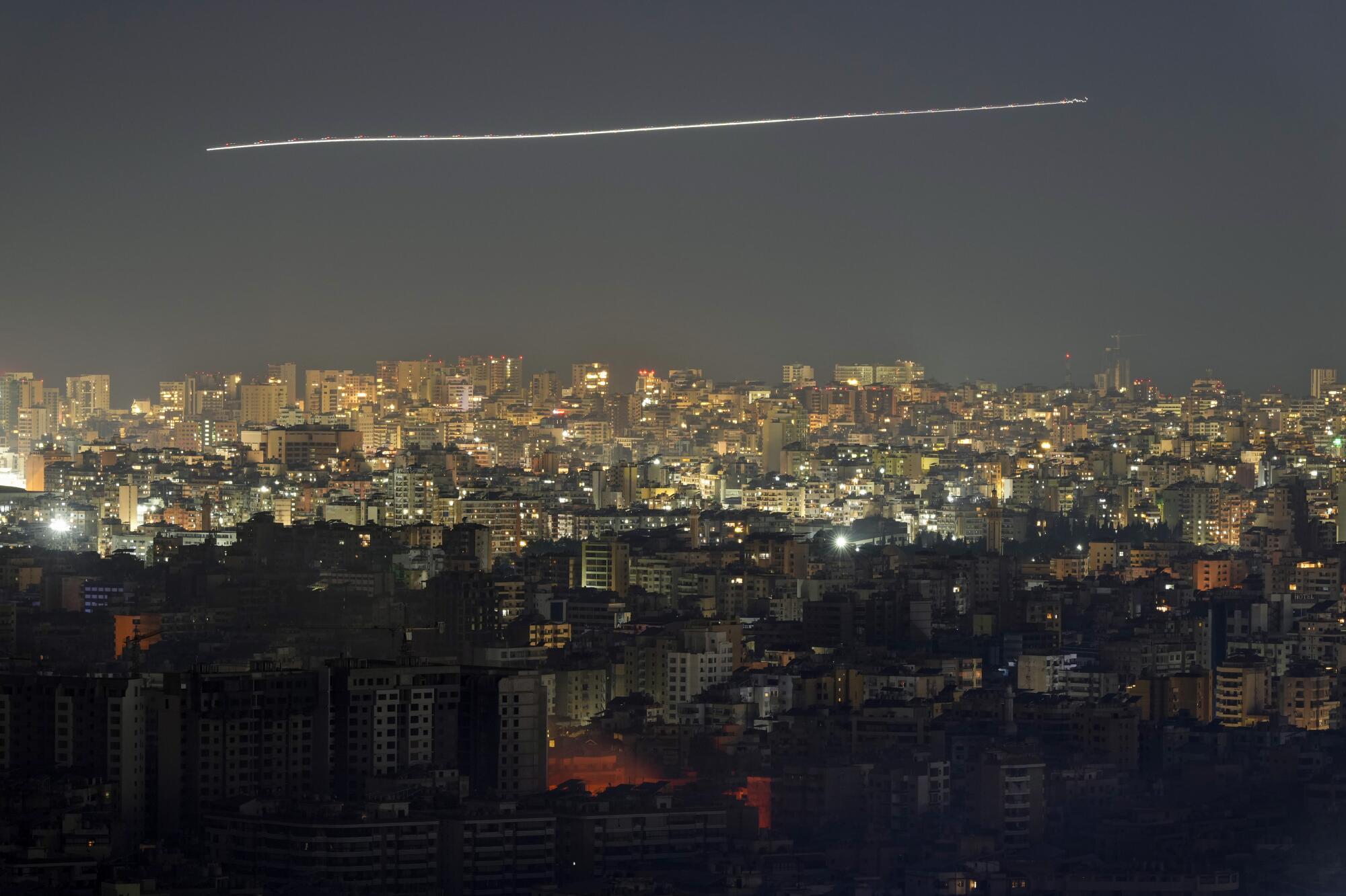 A timed-exposure image shows the contrail of a jet airliner flying over Beirut through smoke from Israeli airstrikes  