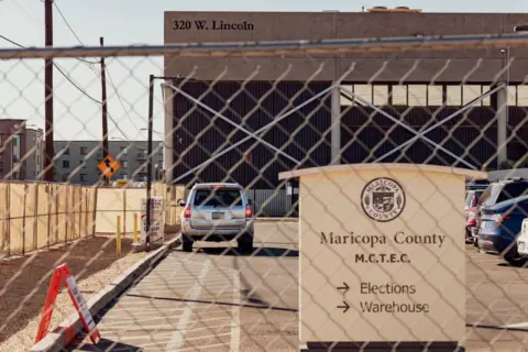 Getty Images Fence and gate in front of parking lot where a sign says "Maricopa County" and has arrows to elections warehouse