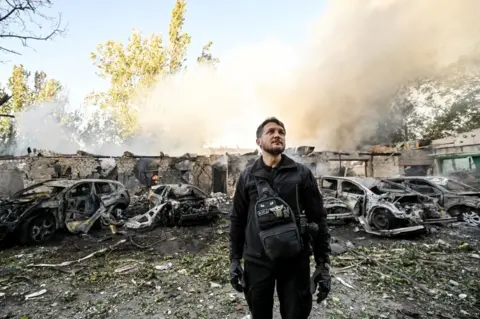 Getty Images A man is pictured against the background of cars destroyed as a result of Russian shelling