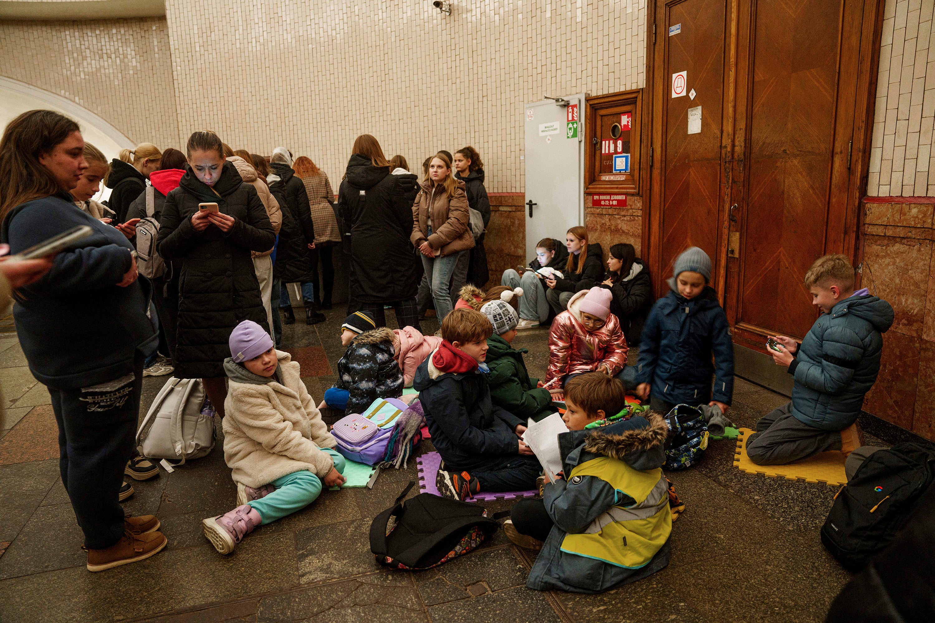 Children sit on a floor inside Arsenalna metro station during air alert in Kyiv, Ukraine