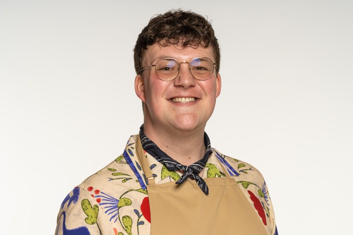 Mike wearing a floral shirt and brown apron, smiling ahead.