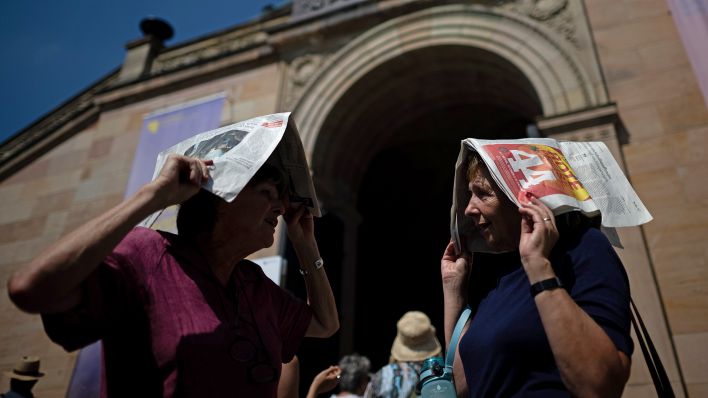 Symbolbild:Zwei Frauen, die vor der Alten Nationalgalerie anstehen schützen sich vor der Hitze mit Zeitungen über den Köpfen.(Quelle:picture alliance/dpa/S.Gollnow)