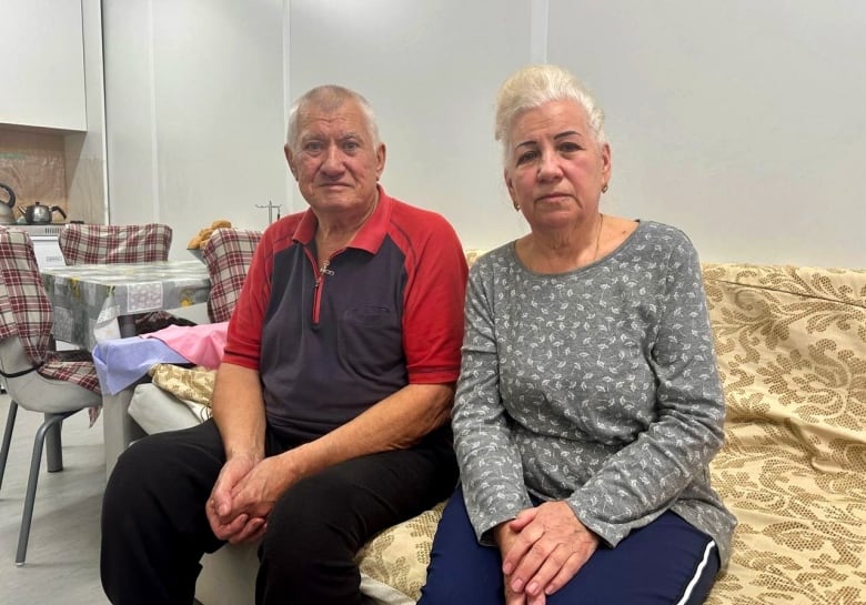 An elderly man and woman sit on a bed.