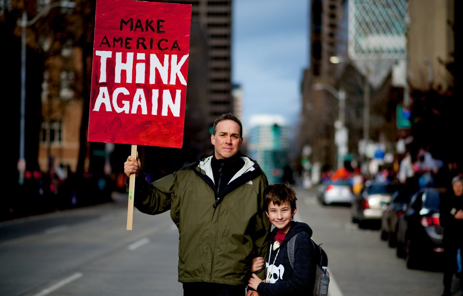 man beside boy holding red and white rally signage